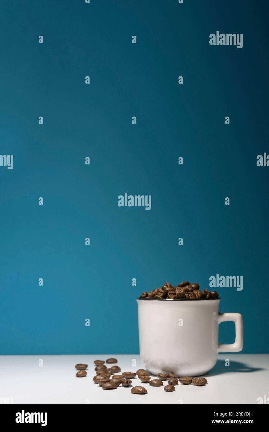 Eine weiße Tasse mit Kaffeebohnen auf dunkelblauem Hintergrund. Vertikales Banner. Modell Stockfoto