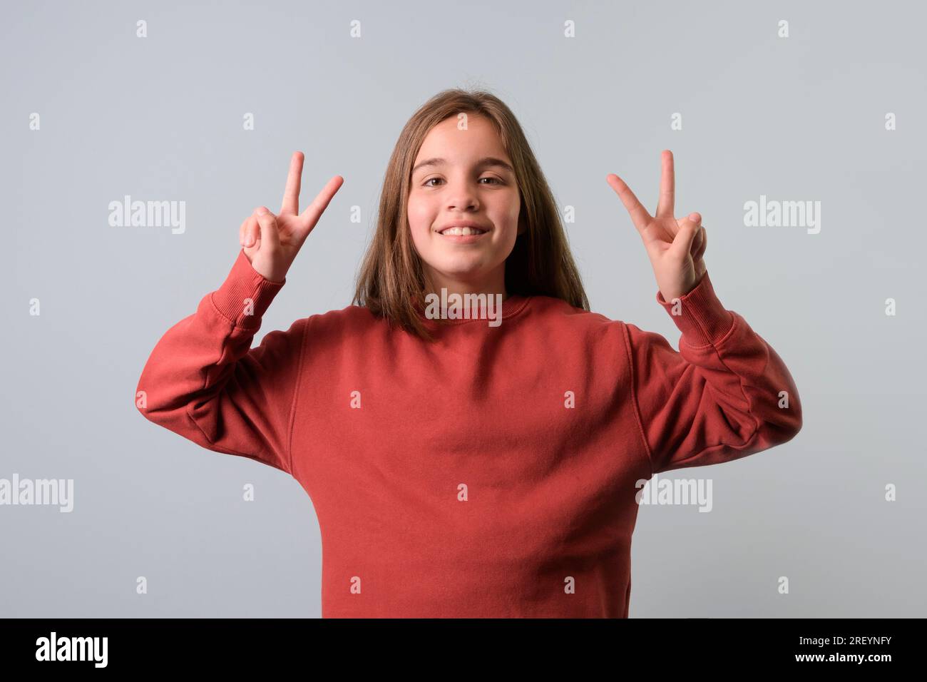 Porträt eines Teenagers, ein Zeichen des Sieges mit den Fingern. Roter Pullover, grauer Hintergrund Stockfoto