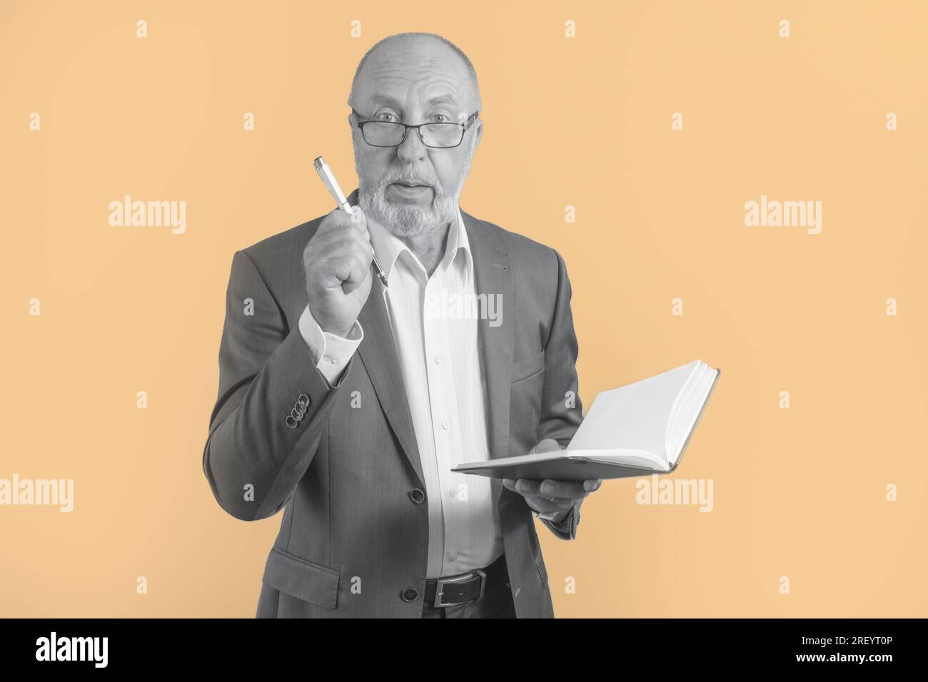 Porträt eines älteren Geschäftsmannes in einem Anzug mit Notizbuch und Kugelschreiber, der in die Kamera schaut - auf pfirsichfarbenem Hintergrund. Schwarz-Weiß-Konzept Stockfoto