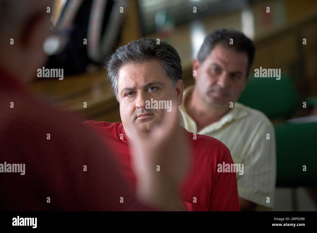 Zwei Männer hören aufmerksam zu, in einem Klassenzimmer, mit einer verschwommenen Geste im Vordergrund. Stockfoto