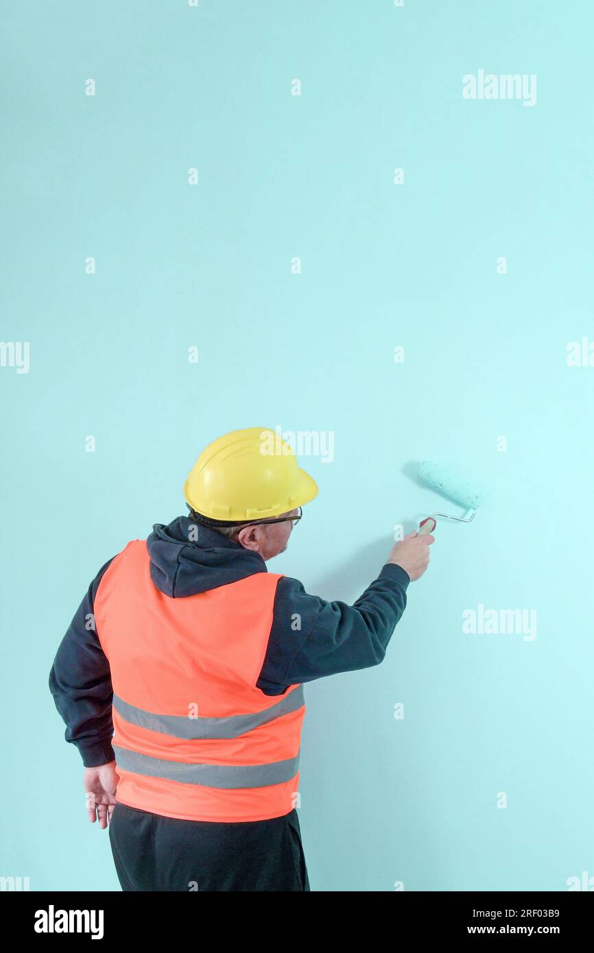 Maler in Uniform und Helm malt eine hellgrüne Wand mit einer Malerwalze. . Vertikales Format. Speicherplatz kopieren Stockfoto