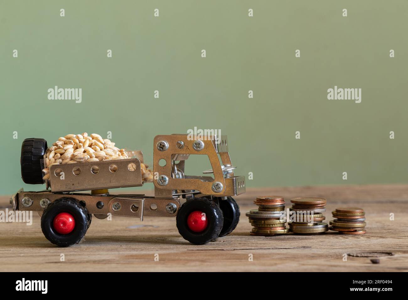 Frachttransport von Getreide auf einer Kinderschreibmaschine von einem Metallkonstruktor auf einer Holzplatte und Münzstapel stehen nebeneinander, Logistik Stockfoto