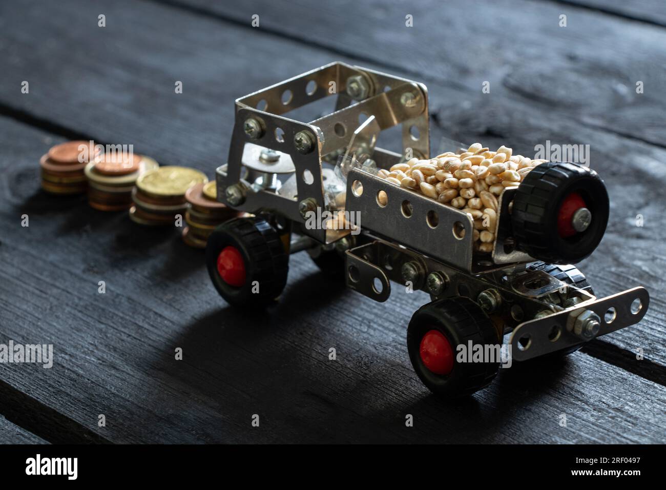 Frachttransport von Getreide auf einer Kinderschreibmaschine von einem Metallkonstruktor auf einer Holzplatte und Münzstapel stehen nebeneinander, Logistik Stockfoto
