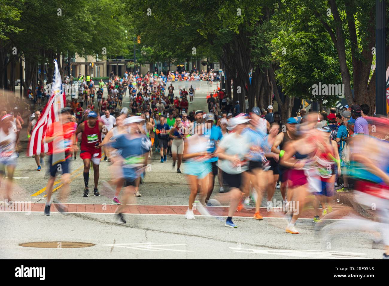 Atlanta, GA/USA – 4. Juli 2023: Motion Blur zeigt einen Mann mit amerikanischer Flagge beim jährlichen Peachtree Road Race am 4. Juli 2023 in Atlanta. Stockfoto