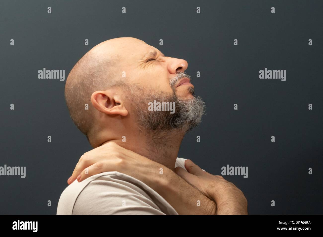 Ein Mann in seinen 50s, emotional erschüttert, der Stress oder Schmerz zeigt. Schwächegefühl oder Depression. Isoliert auf dunklem Hintergrund. Stockfoto