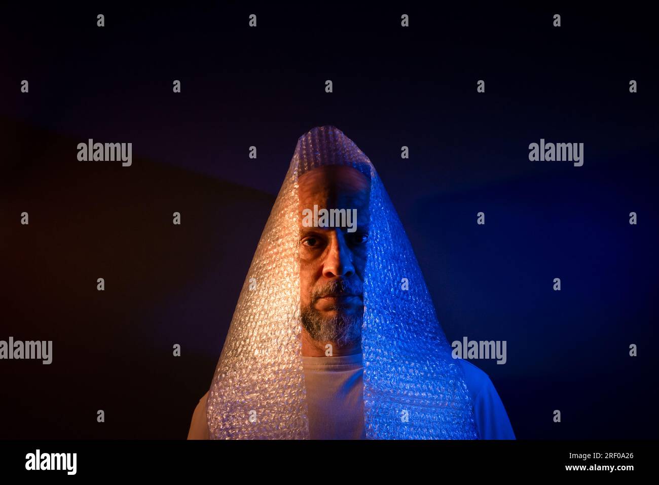 Glatzkopf mit Bart und Luftpolsterfolie um den Kopf. Isoliert auf dunkelrotem Hintergrund. Stockfoto