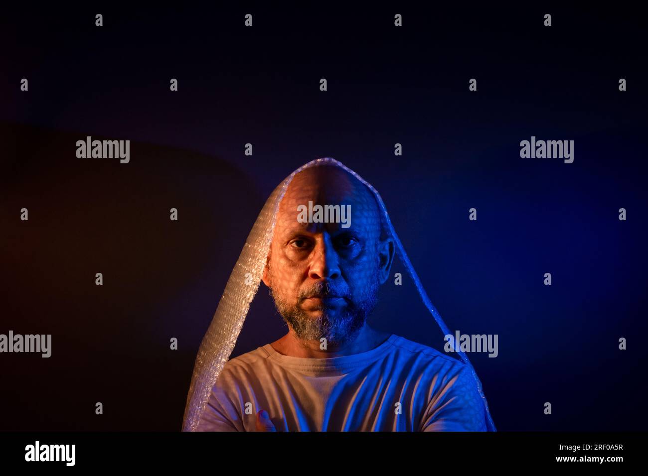 Glatzkopf mit Bart und Luftpolsterfolie um den Kopf. Isoliert auf dunkelrotem Hintergrund. Stockfoto