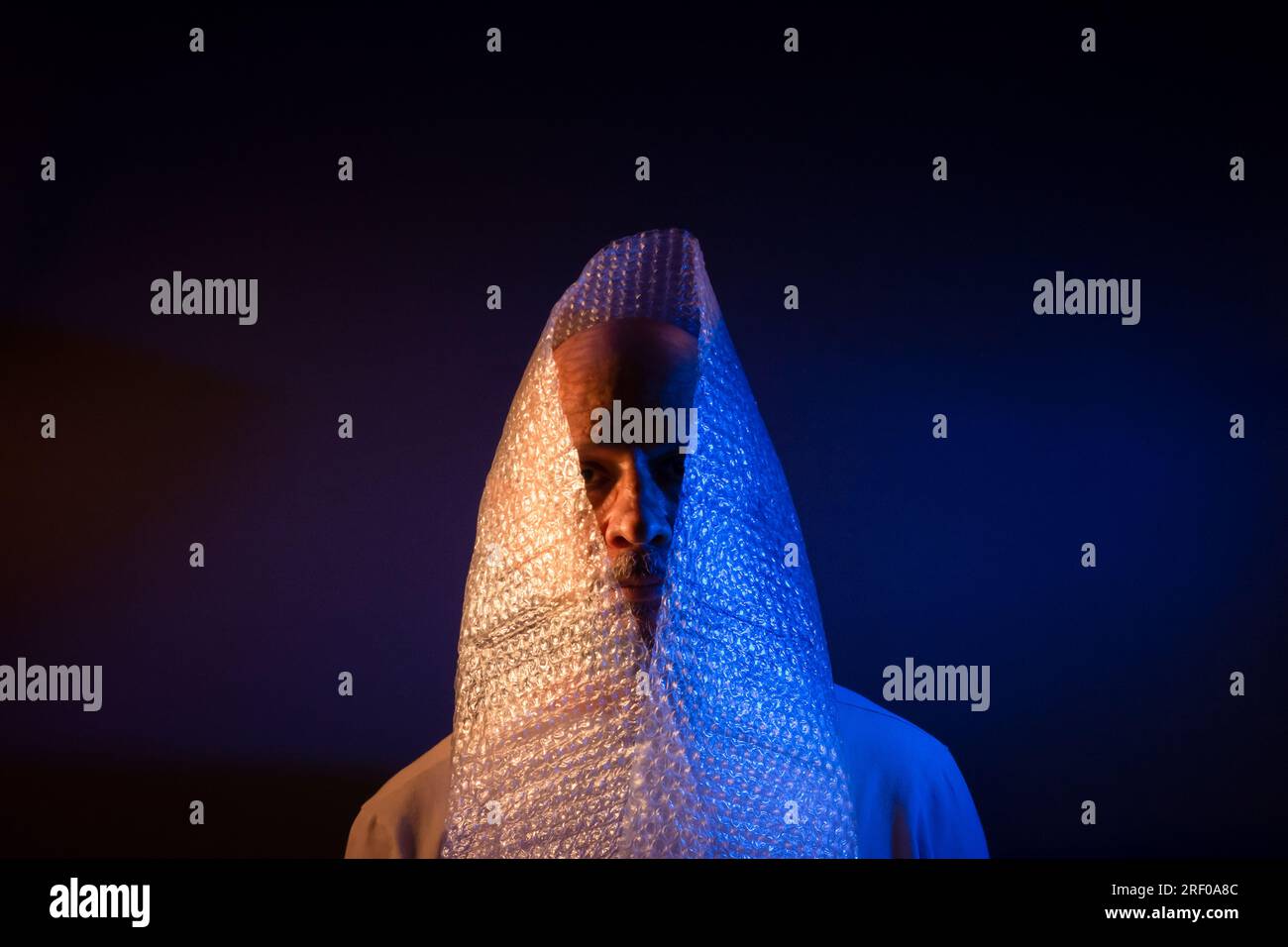 Glatzkopf mit Bart und Luftpolsterfolie um den Kopf. Isoliert auf dunkelrotem Hintergrund. Stockfoto