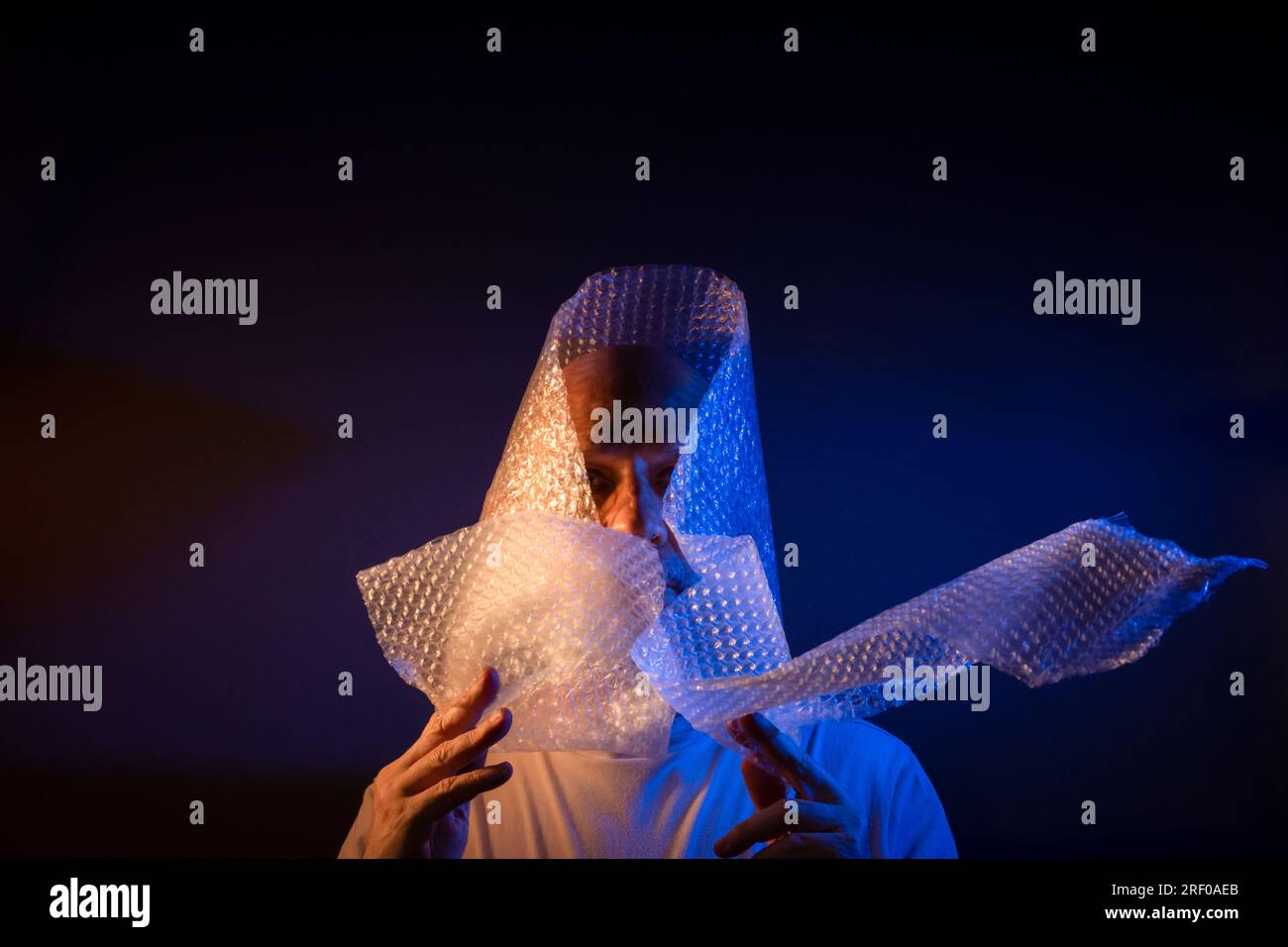 Glatzkopf mit Bart und Luftpolsterfolie um den Kopf. Isoliert auf dunkelrotem Hintergrund. Stockfoto