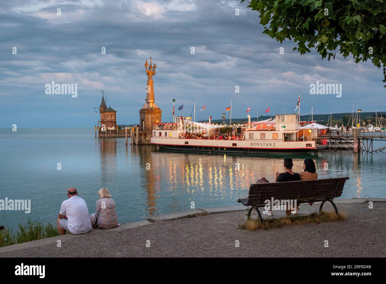 Menschen, die sich am Ufer des Bodensees entspannen, den Blick über den Hafen genießen, Imperia Statue in Sicht, Konstanz, Baden-Württemberg, Deutschland Stockfoto