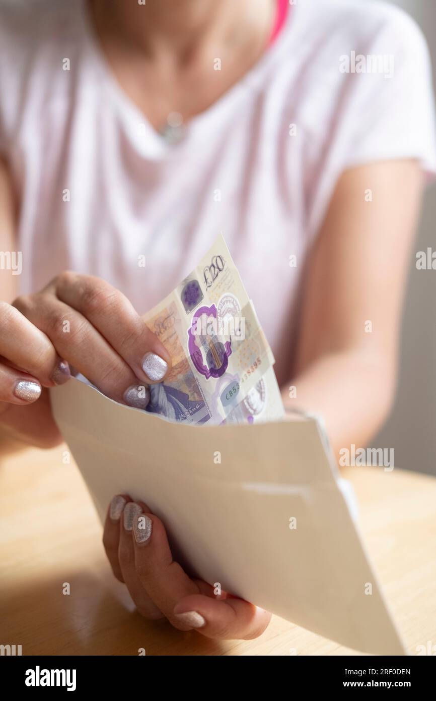 Eine Frau, die Geld aus einem Umschlag nimmt, spart Geld, spart Lebenshaltungskosten, 20 Krawatten, 20 Pfund Sterling-Banknoten Stockfoto