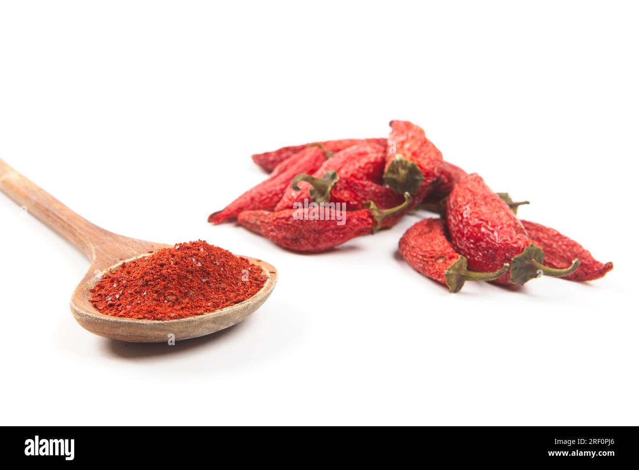 Nahaufnahme des Stilllebens von rotem Pfefferpulver in einem Holzlöffel neben teilweise getrockneten roten Paprika. Stockfoto