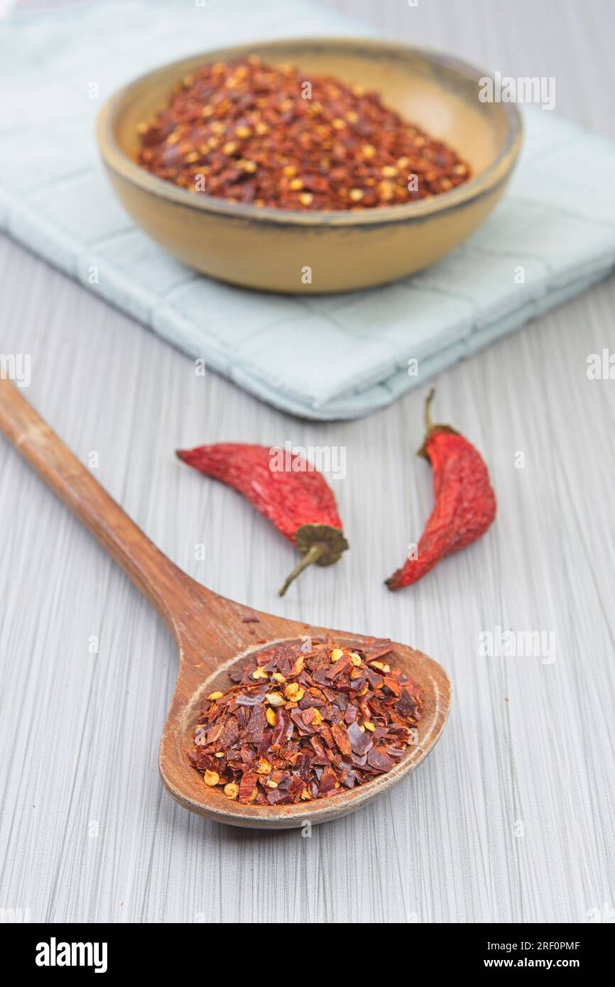 Studiofoto von roten Pfefferflocken auf einem Holzlöffel mit einer gelben Holzschüssel mit Pfefferpulver und rotem Paprika. Stockfoto