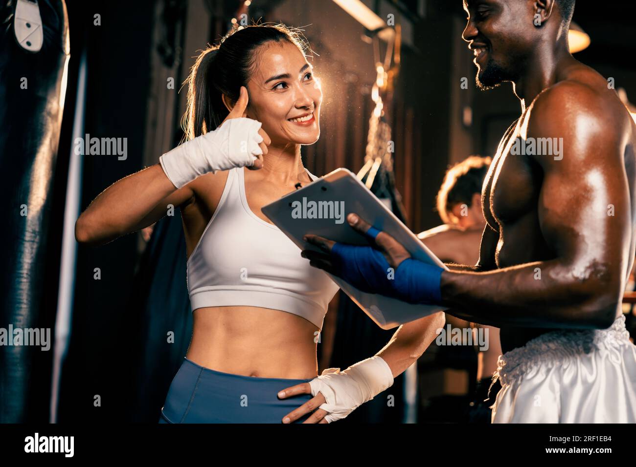 Eine asiatische Muay Thai-Boxerin und ihr persönlicher Boxtrainer diskutieren über ihren körperlichen Fortschritt im Fitnessstudio, der die Bindung an ihre Körpermuskulatur widerspiegelt Stockfoto