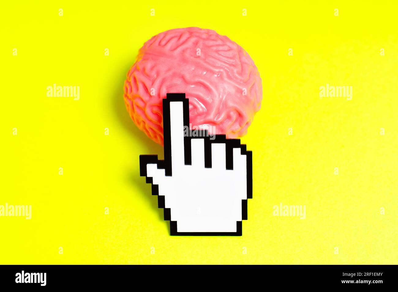 Plastisch verpixelter Hand-Cursor klickt auf ein pinkfarbenes menschliches Gehirnmodell, isoliert auf einem gelben Hintergrund. Stockfoto