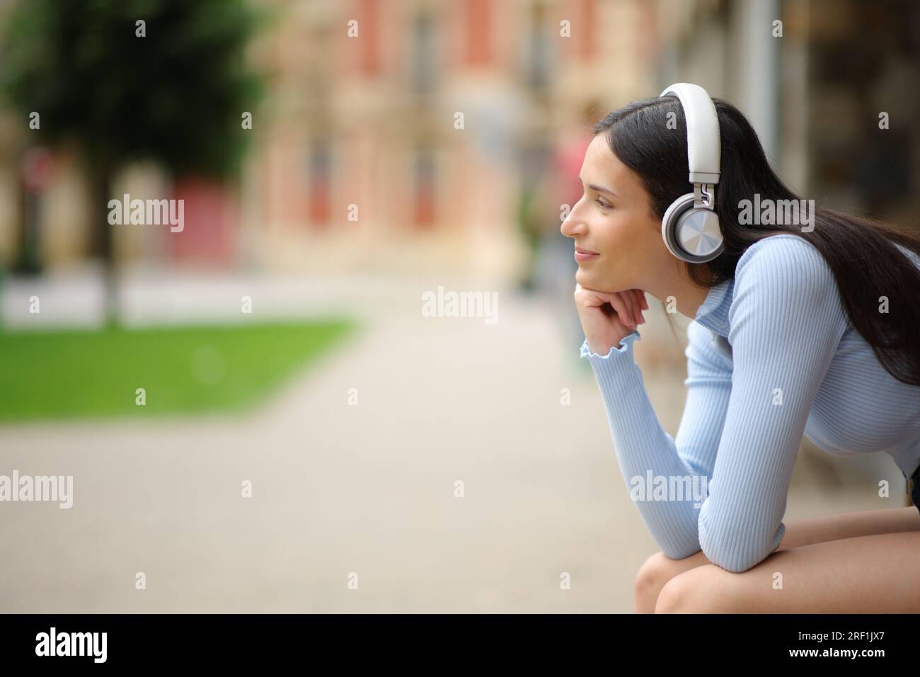 Profil einer Frau mit Kopfhörern, die entspannt auf einer Bank sitzt und Musik auf der Straße hört Stockfoto