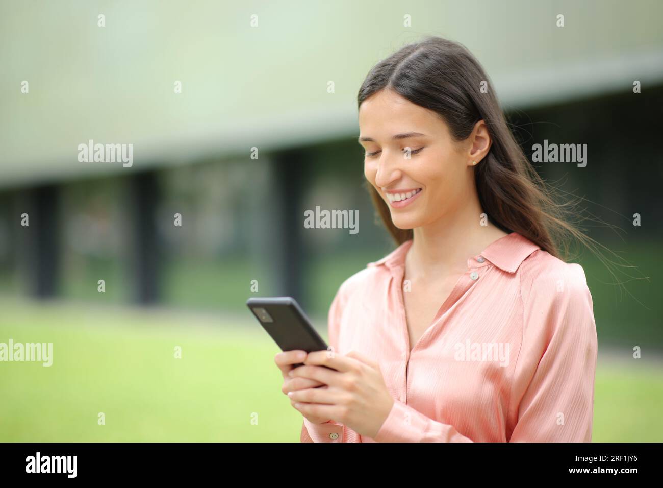 Alleinstehende, glückliche Frau, die mit dem Handy in einem Park spaziert Stockfoto