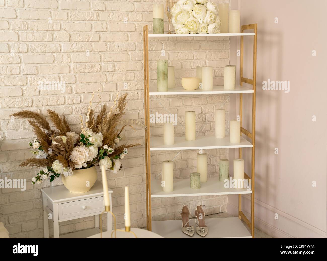 Hochzeitszimmer. Auf dem Regal liegt ein weißer Strauß aus Brautblumen, Kerzen, Gläsern und Schuhen. Wunderschöner Hintergrund. Stockfoto