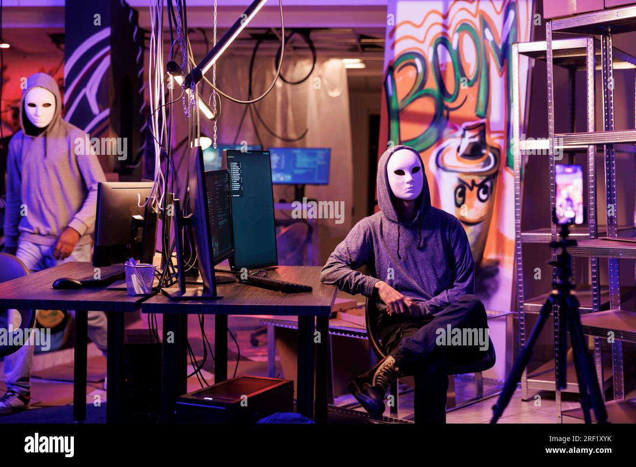 Anonymer Hacker in Masken, der ein Bedrohungsvideo auf einer Smartphone-Kamera in einem verlassenen Lagerhaus aufnimmt. Cyberkriminelle brechen Gesetze, während sie Internetbetrug und Cyberangriffe auf Mobiltelefone streamen Stockfoto
