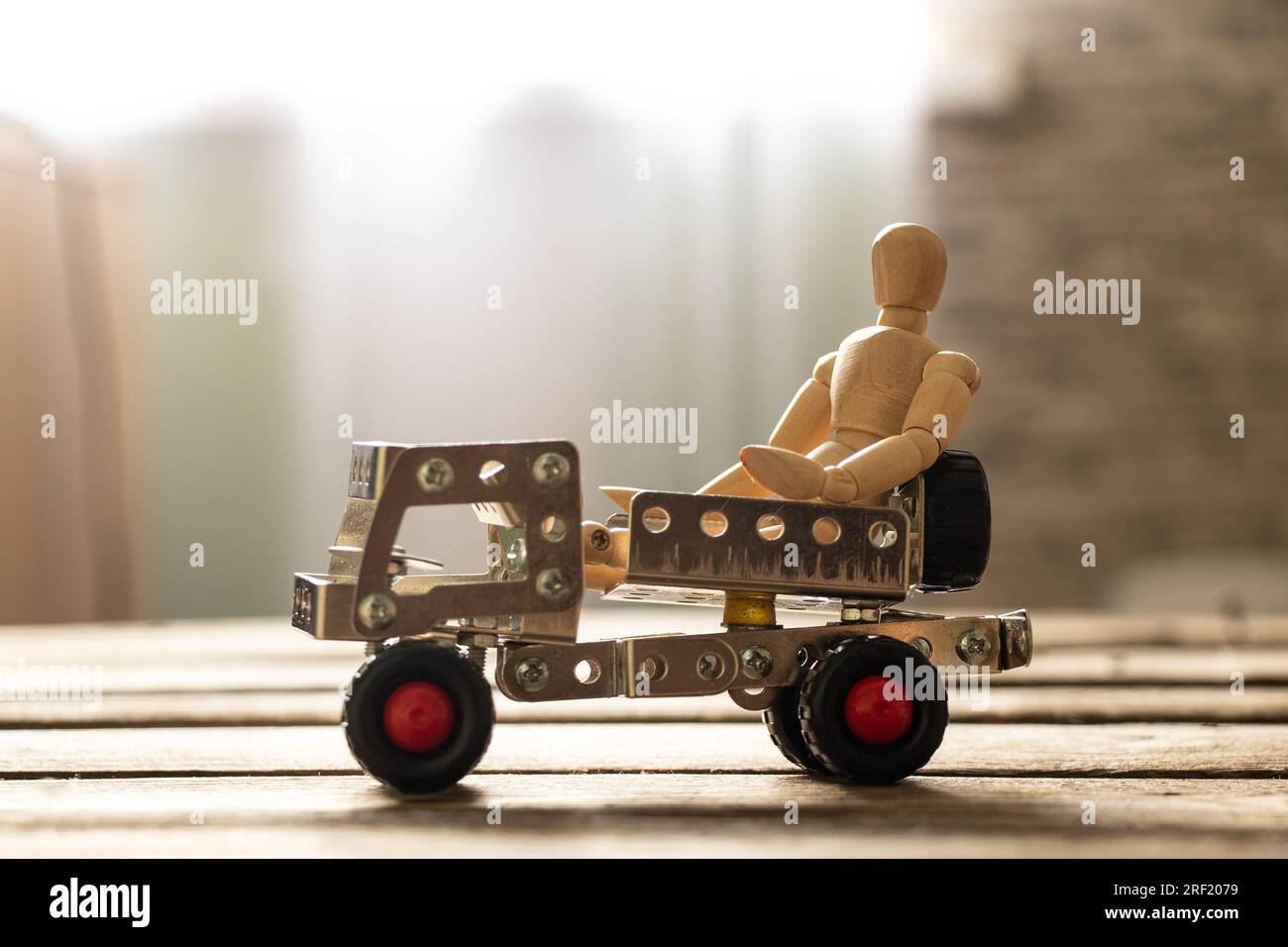Ein kleiner Mann aus Holz sitzt auf einer Schiene aus Metallklötzen auf einem Holzbrett, Kinderspielzeug und Transportmitteln Stockfoto