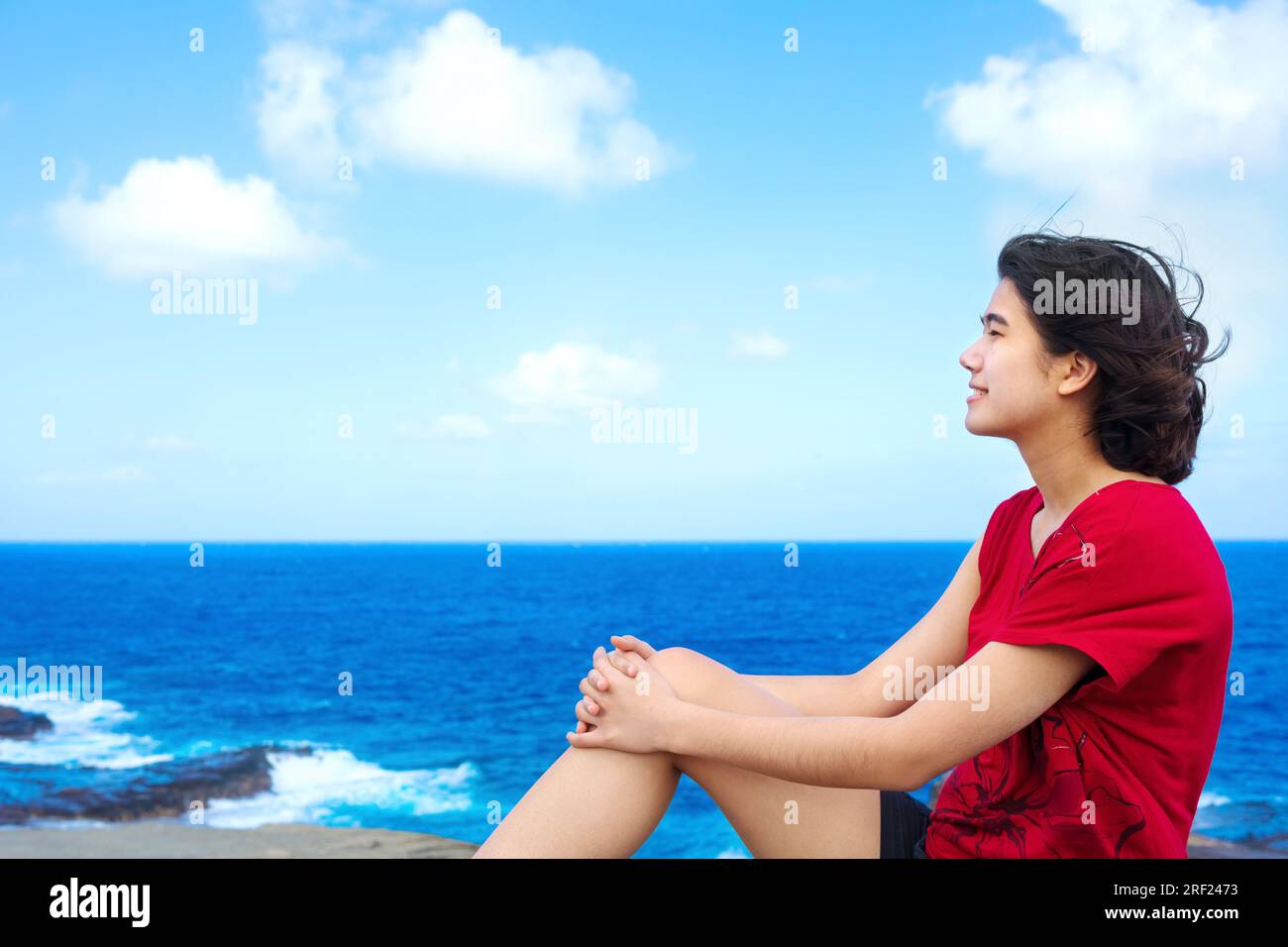 Junge Frau, die auf einer großen Felsenklippe am hawaiianischen Ozean sitzt und über den Horizont blickt Stockfoto