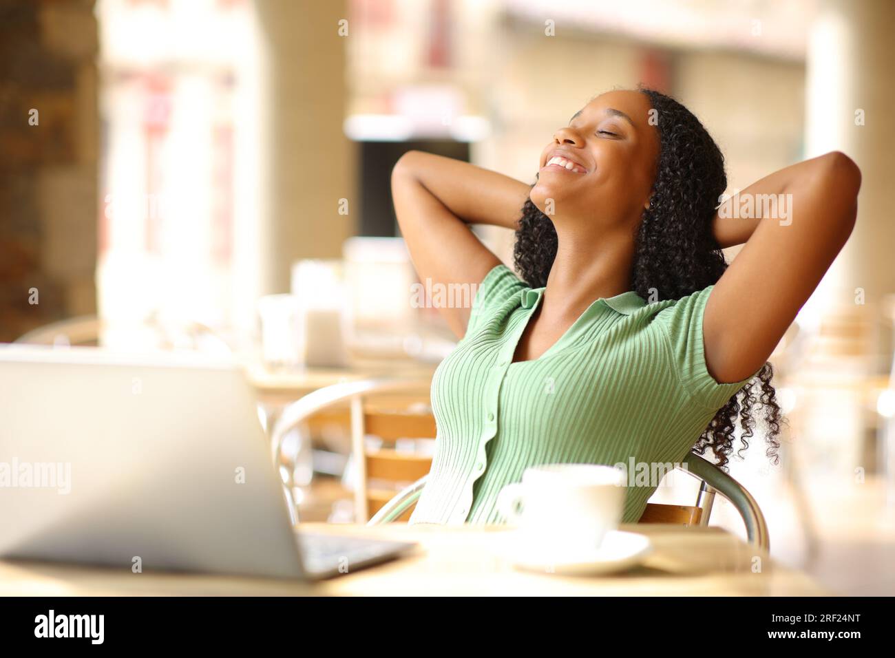 Schwarze Frau mit Laptop, die sich auf einer Barterrasse entspannen kann Stockfoto