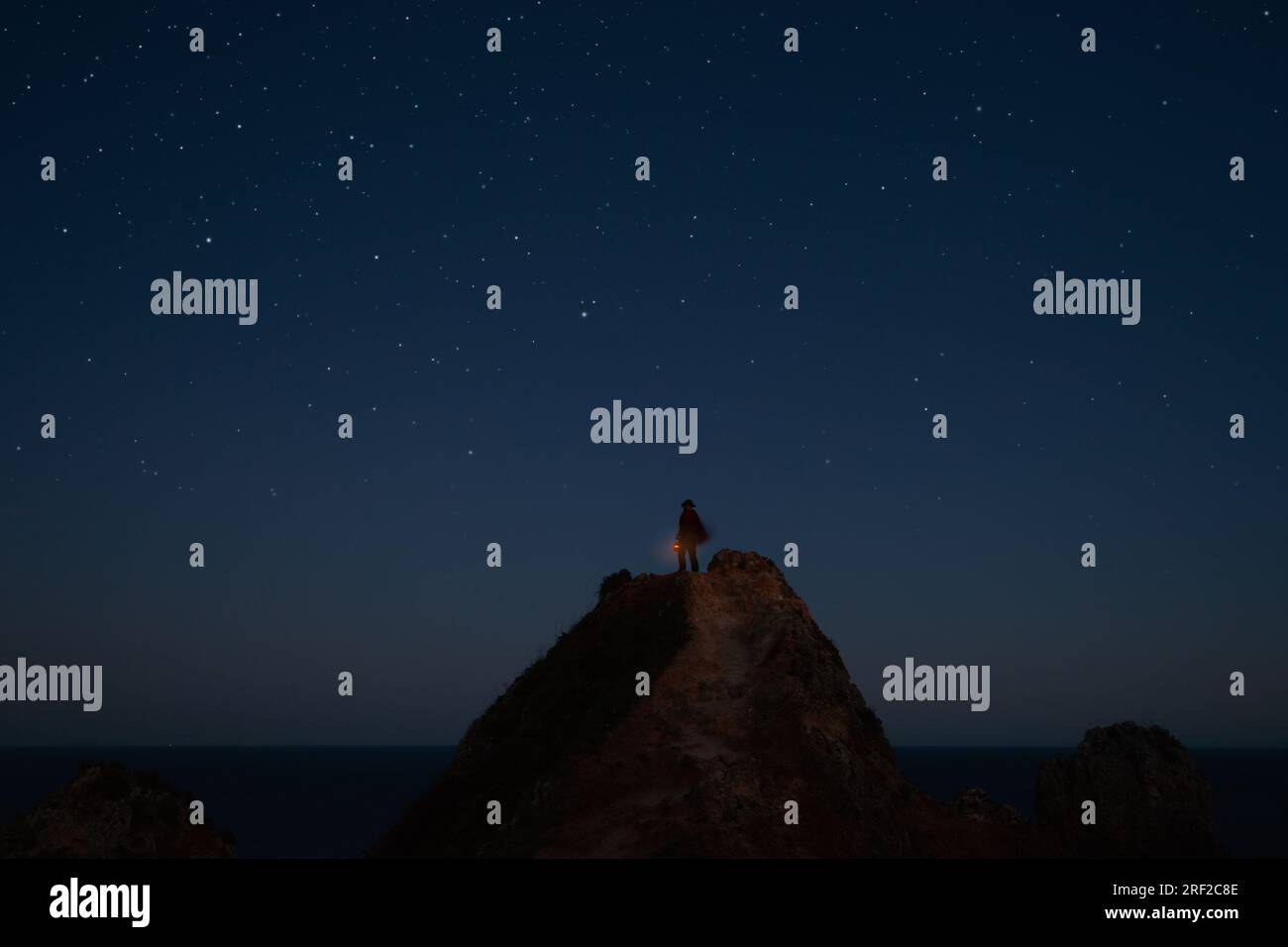 Mann mit Laterne auf dem Gipfel des Berges über dem dunklen Sternenhimmel. Stockfoto