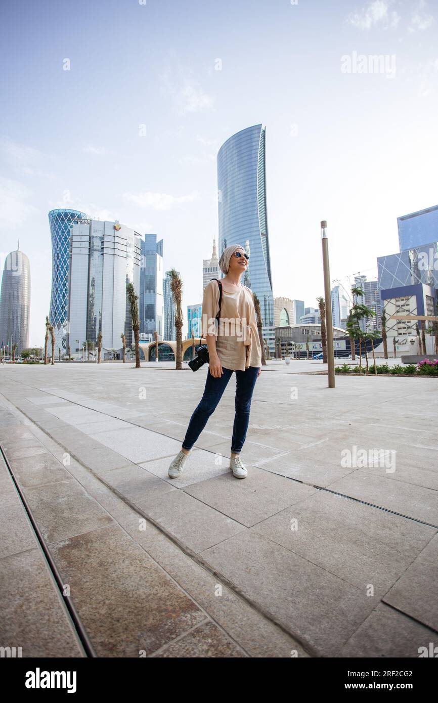 Junge Frau steht vor Wolkenkratzern in Doha Stockfoto
