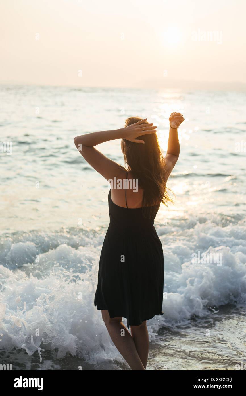 Rückansicht einer Frau, die bei Sonnenuntergang im flachen Meer steht Stockfoto