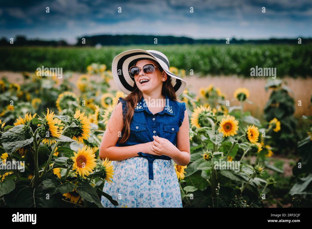 Mädchen mit Sonnenbrille und Strohhut, die auf einem Sonnenblumenfeld lachen Stockfoto