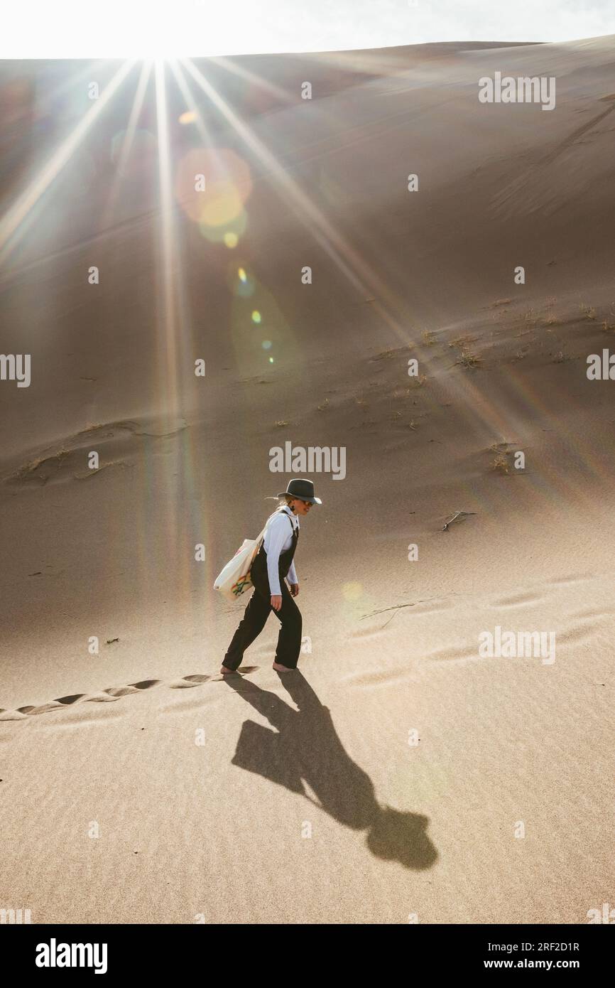 Eine einsame Frau wandert durch Sanddünen mit Overalls und Sonnenschein Stockfoto