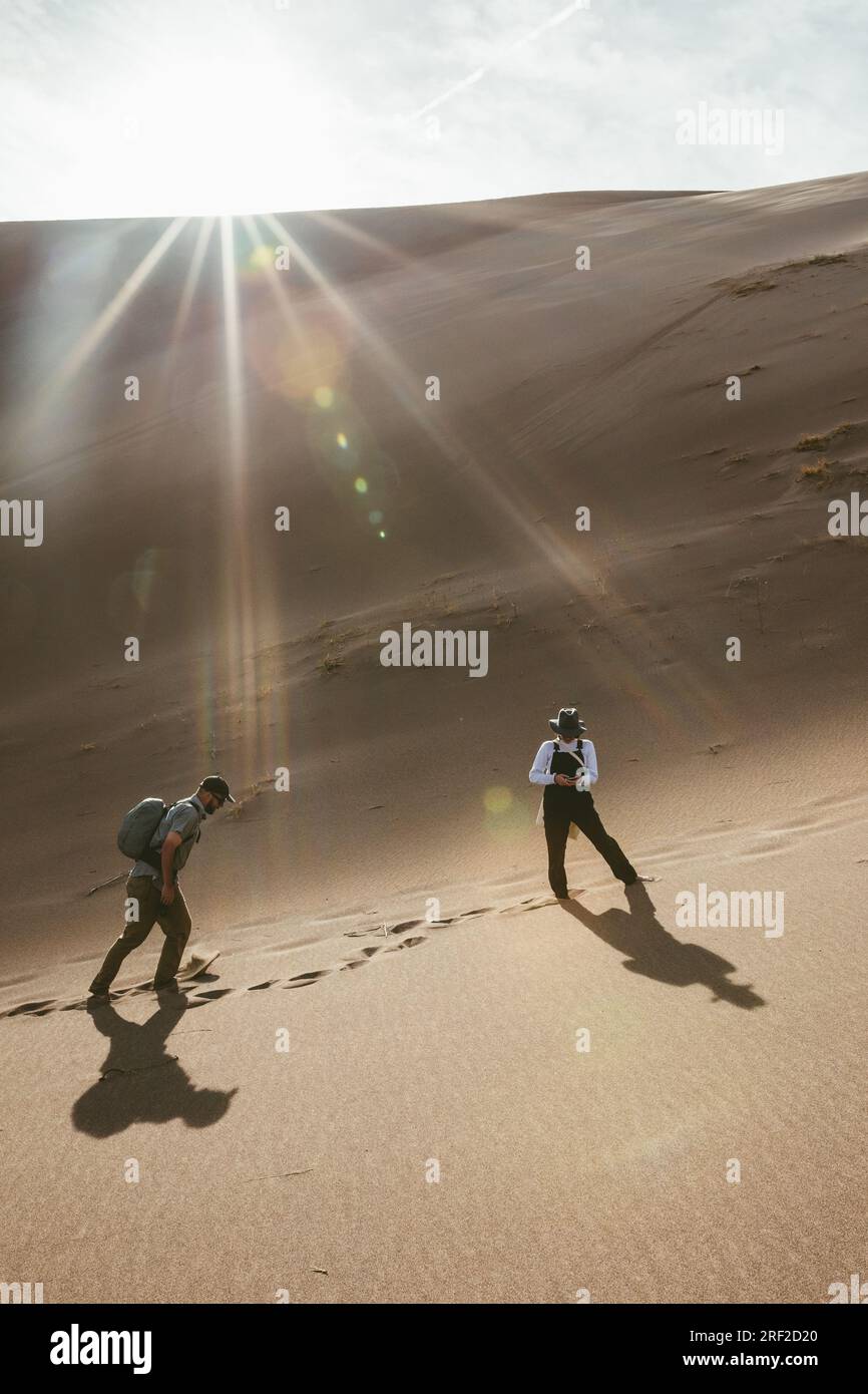 Eine Frau schaut auf ihr Handy und wartet auf einen männlichen Begleiter, der in den Dünen wandert Stockfoto