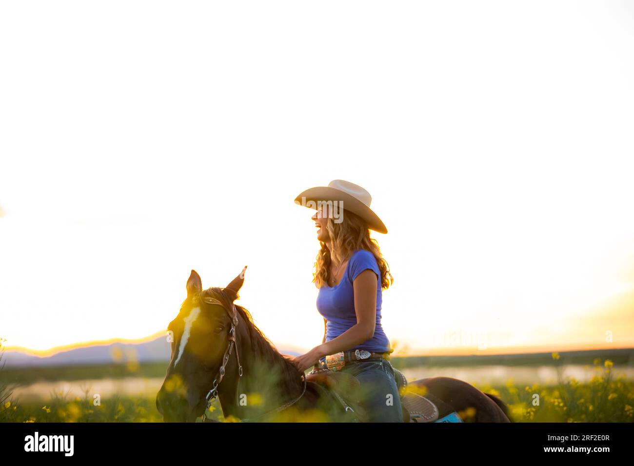 Zwanzig Jahre altes Cowgirl, das bei Sonnenuntergang auf dem Pferderücken lacht Stockfoto