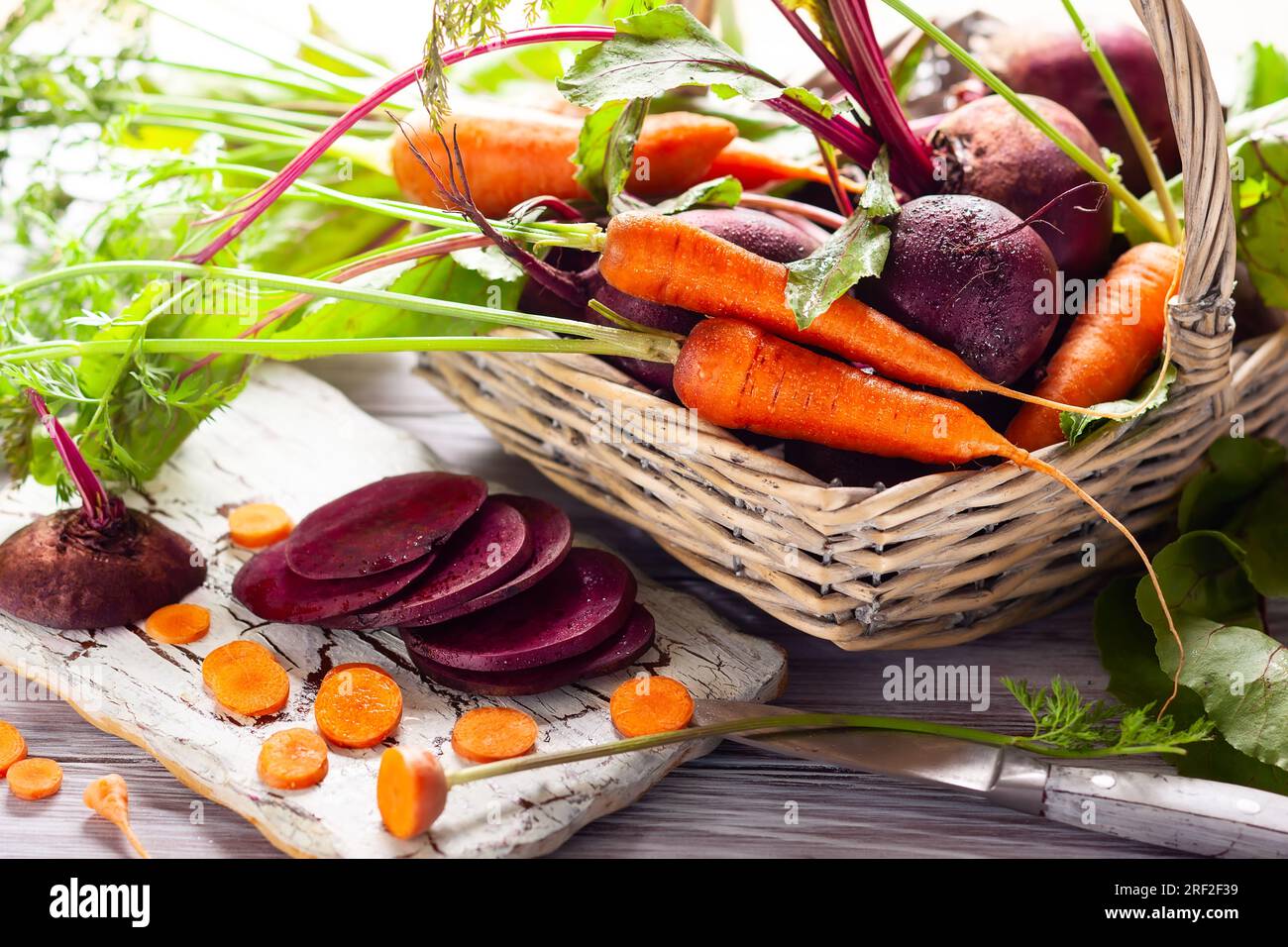 Frische Bio-Rote Bete und Karotten mit grünen Blättern in einem Korb auf einem braunen Holztisch. Stockfoto