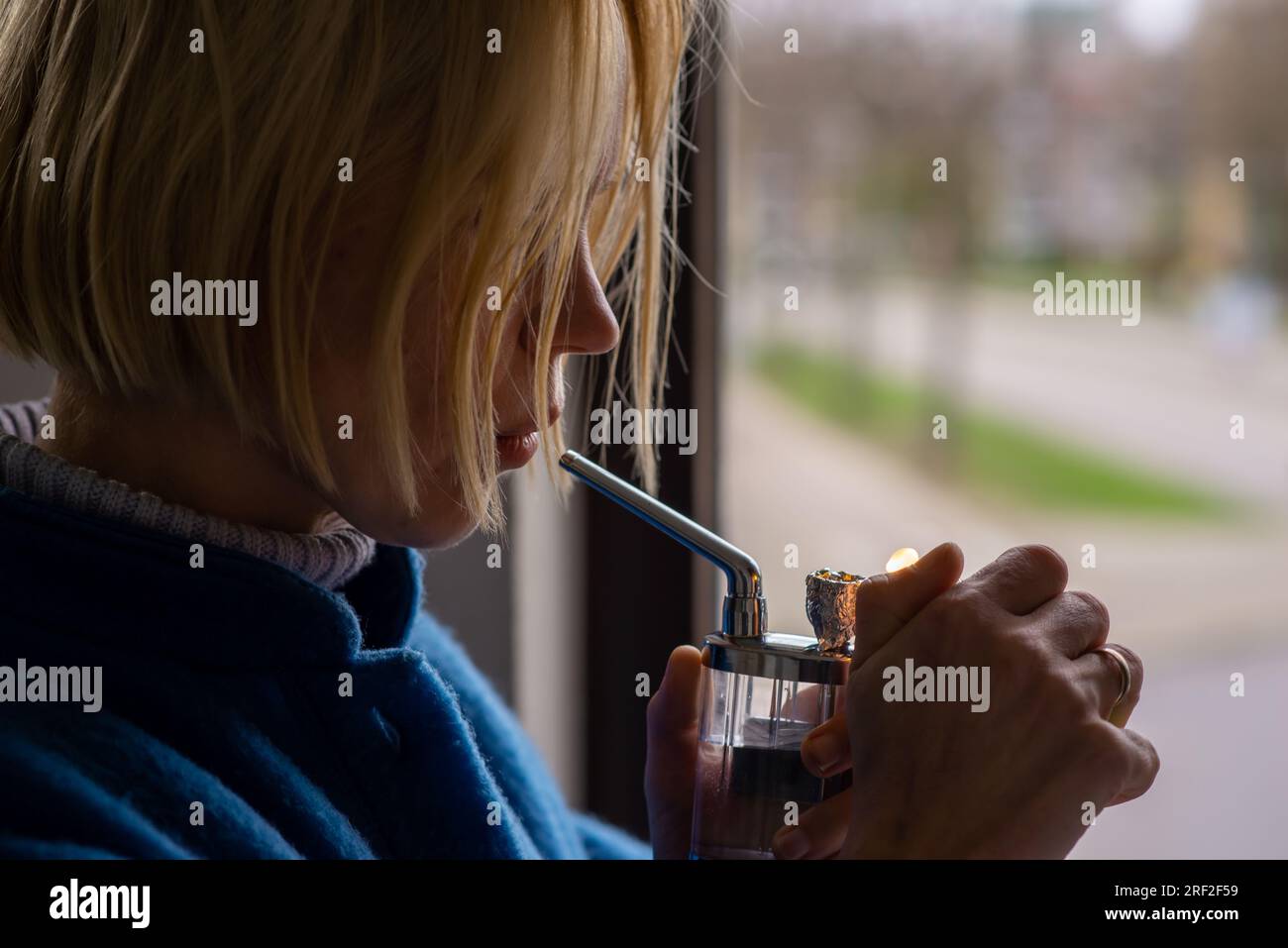 Eine Frau raucht Marihuana, Cannabis. Eine Erwachsene Frau mit blonden Haaren zündet ein Rauchergerät an. Entspannung, ärztliche Verschreibung. Stockfoto