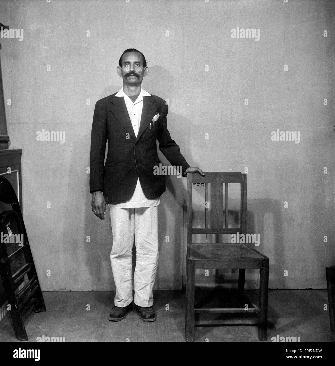 Altes, klassisches Schwarz-Weiß-Bild aus dem Jahr 1900er von einem indischen Mann, lustiges Studioporträt, das einen Mantel-Stuhl trägt und Indien 1940er zeigt Stockfoto