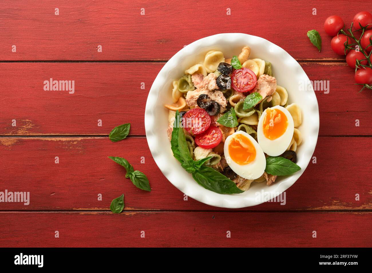 Italienischer Nudelsalat. Orekchiette Pasta mit Thunfisch, Tomatenkirsche, Oliven, Basilikum und Parmesan auf einem roten, alten rustikalen Tischhintergrund. Traditi Stockfoto