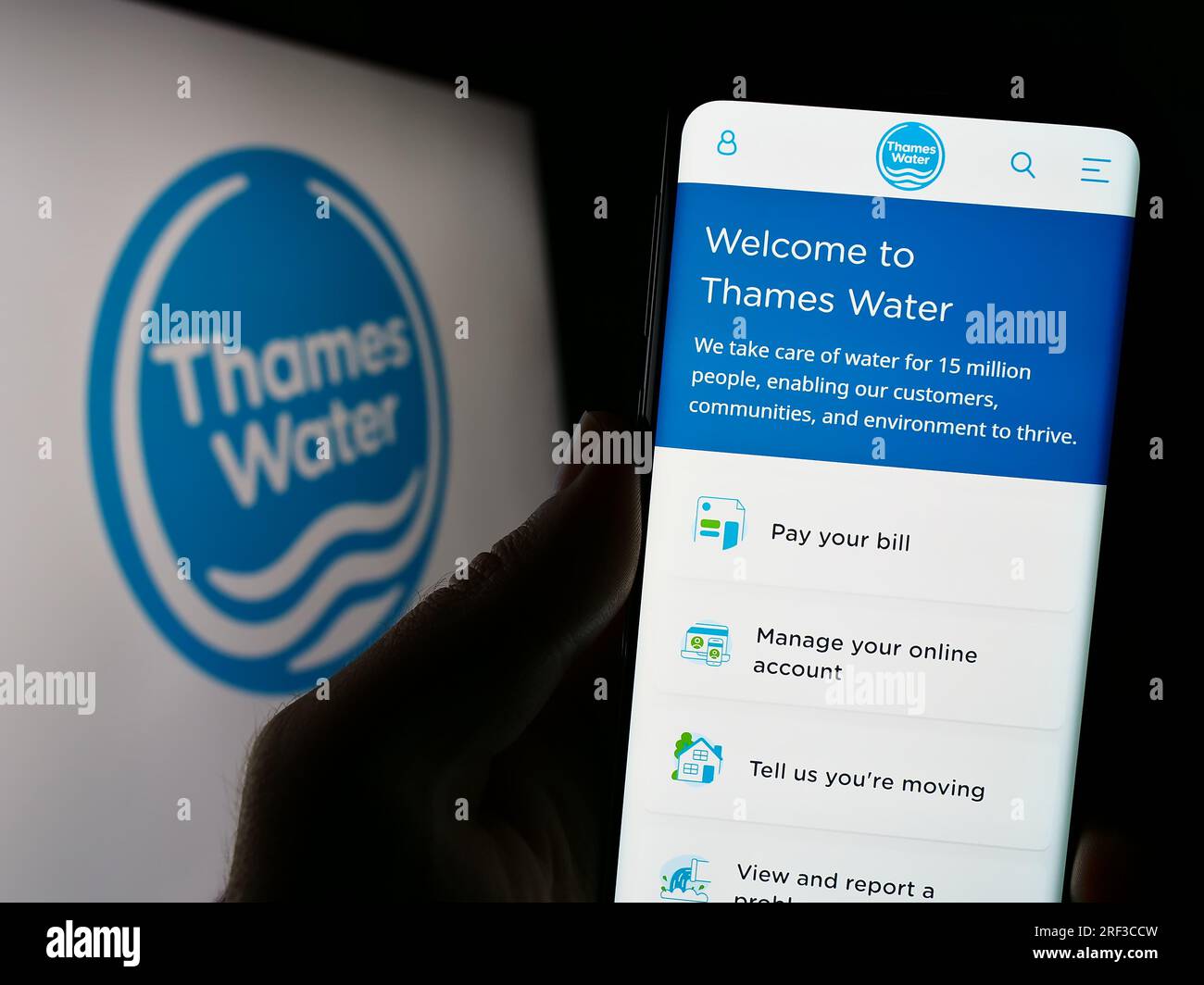 Person, die ein Mobiltelefon mit einer Webseite des britischen Unternehmens Thames Water Utilities Limited auf dem Bildschirm mit Logo hält. Konzentrieren Sie sich auf die Mitte des Telefondisplays. Stockfoto