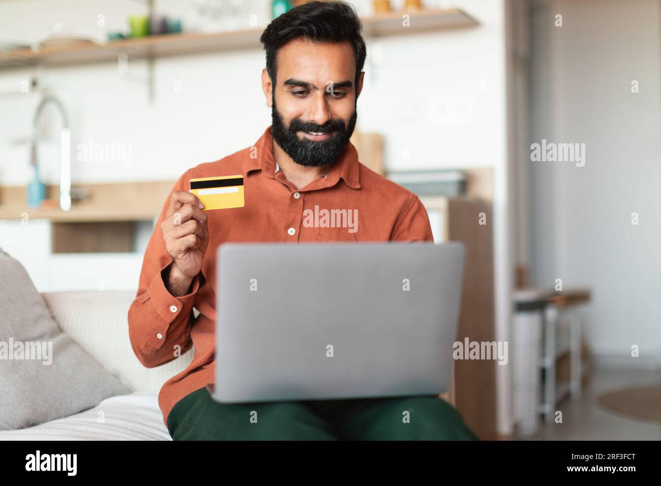 Arabischer Mann mit Laptop und Kreditkarte, der im Haus bezahlt Stockfoto