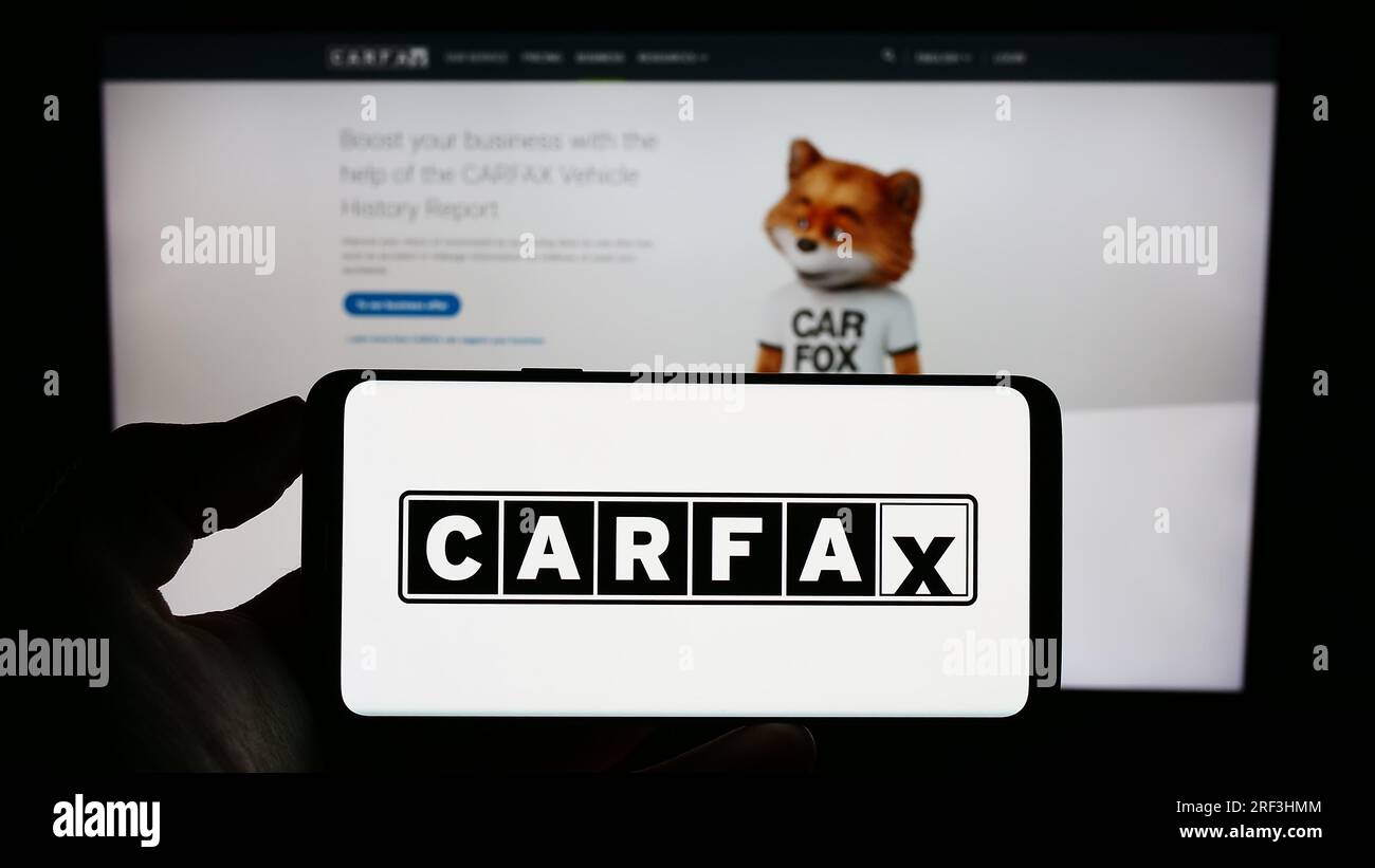 Person, die ein Mobiltelefon mit dem Logo des amerikanischen Fahrzeugdatenunternehmens CARFAX Inc. Auf dem Bildschirm vor der geschäftlichen Webseite hält. Konzentrieren Sie sich auf das Display des Telefons. Stockfoto