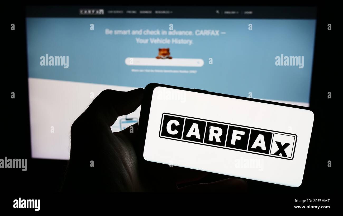 Person, die ein Mobiltelefon mit dem Logo des US-amerikanischen Fahrzeugdatenunternehmens CARFAX Inc. Auf dem Bildschirm vor der geschäftlichen Webseite hält. Konzentrieren Sie sich auf das Display des Telefons. Stockfoto