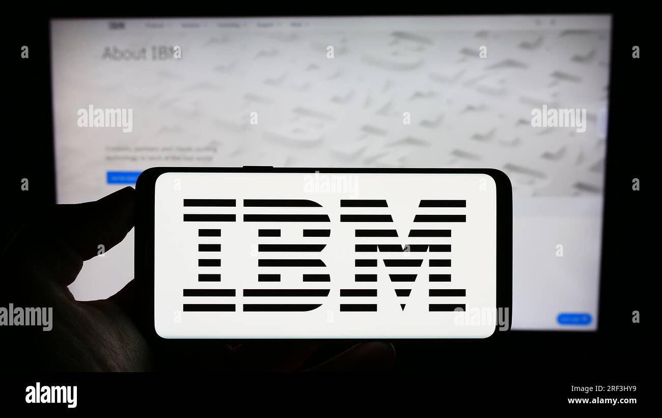 Person, die ein Mobiltelefon mit dem Logo der International Business Machines Corporation (IBM) auf dem Bildschirm vor der Webseite hält. Konzentrieren Sie sich auf das Display des Telefons. Stockfoto