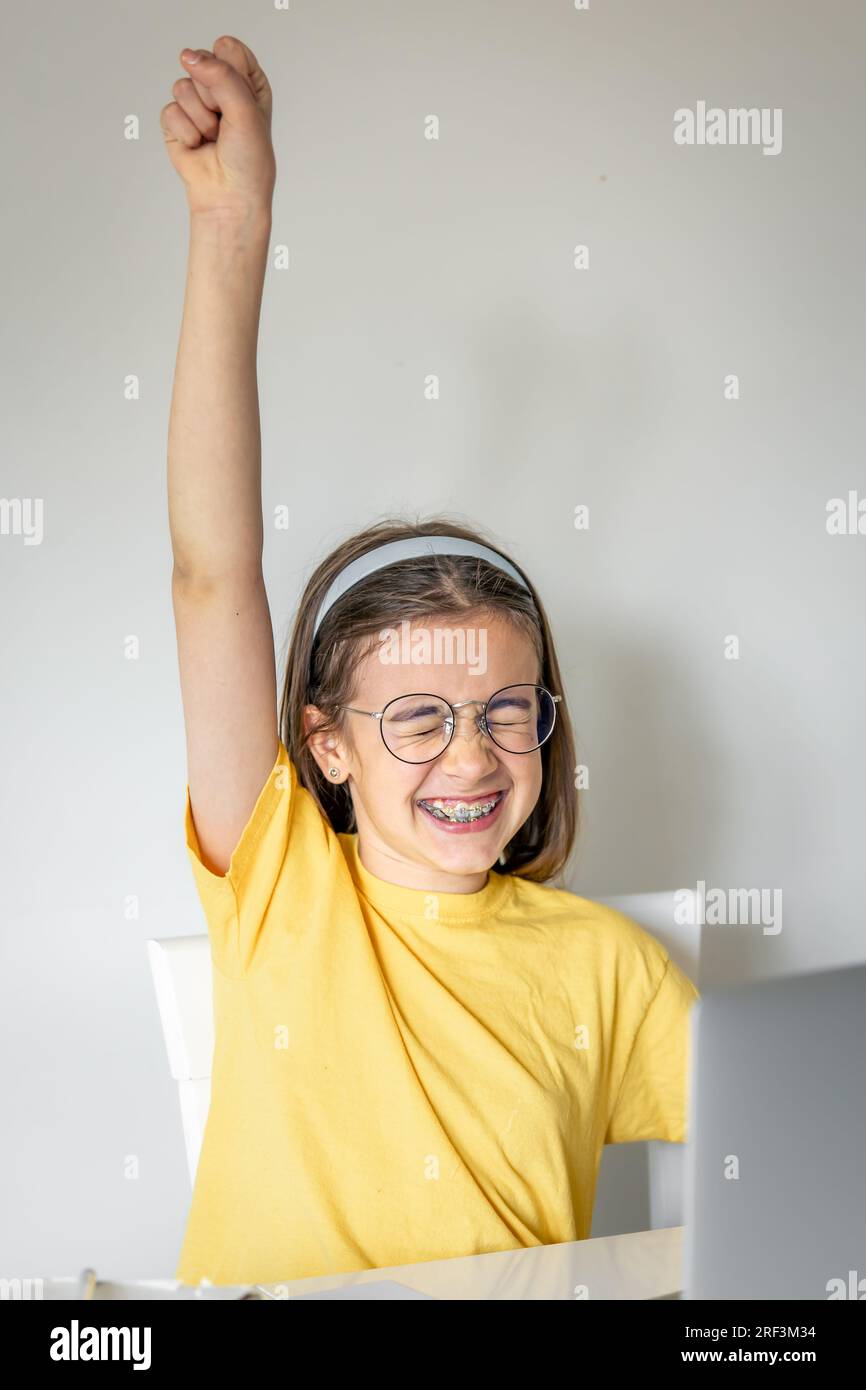 Süßes Schulmädchen mit einem Laptop, das zu Hause lernt, online lernt. Stockfoto