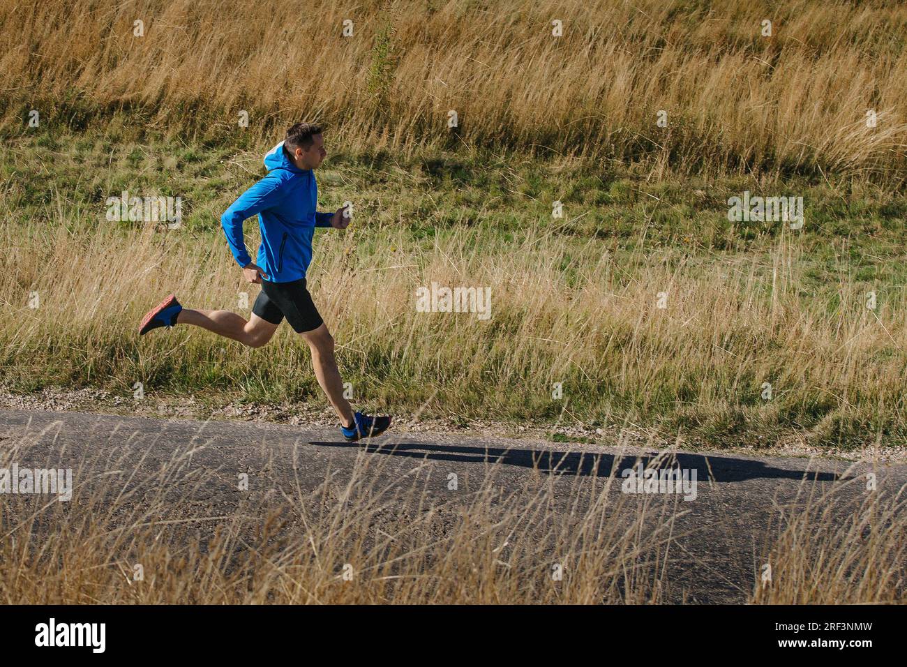 Männlicher Läufer mittleren Alters in blauer Jacke Laufstrecke auf trockenem Gras Stockfoto