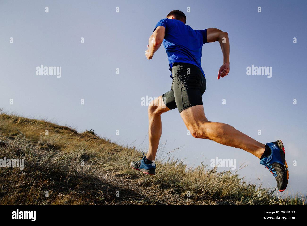 Sportler, der bergauf läuft, in blauem Shirt und schwarzen Strumpfhosen, Hintergrund des Himmels Stockfoto
