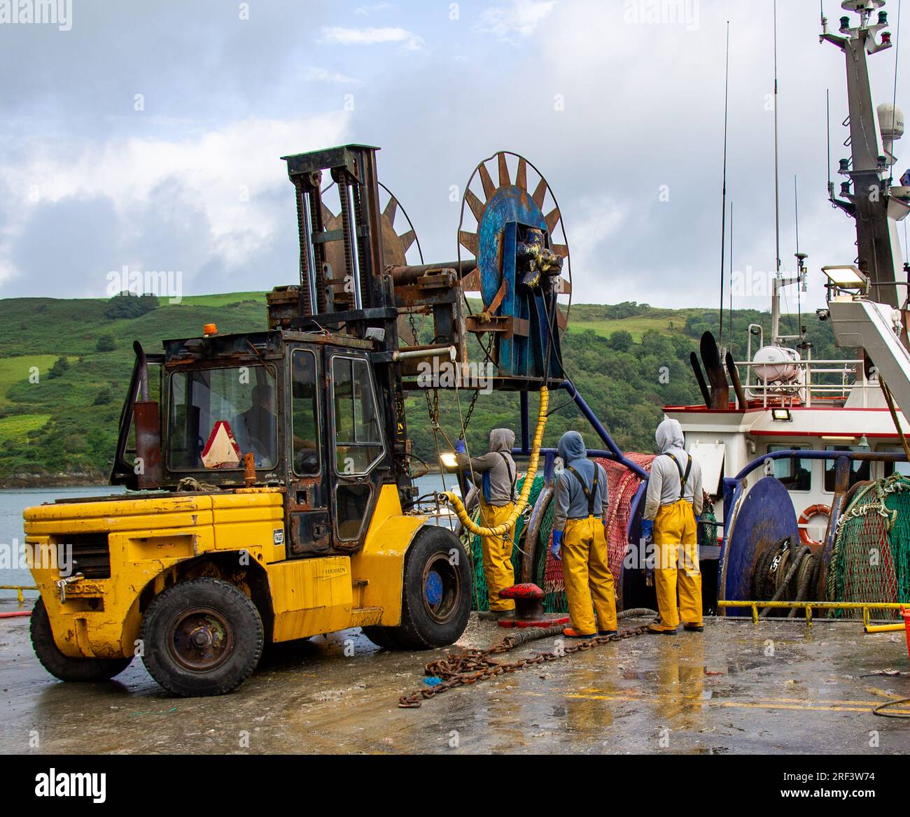 Fischer, die Netze mit Gabelstaplern und hydraulischen Rollen auf einen Trawler laden. Stockfoto