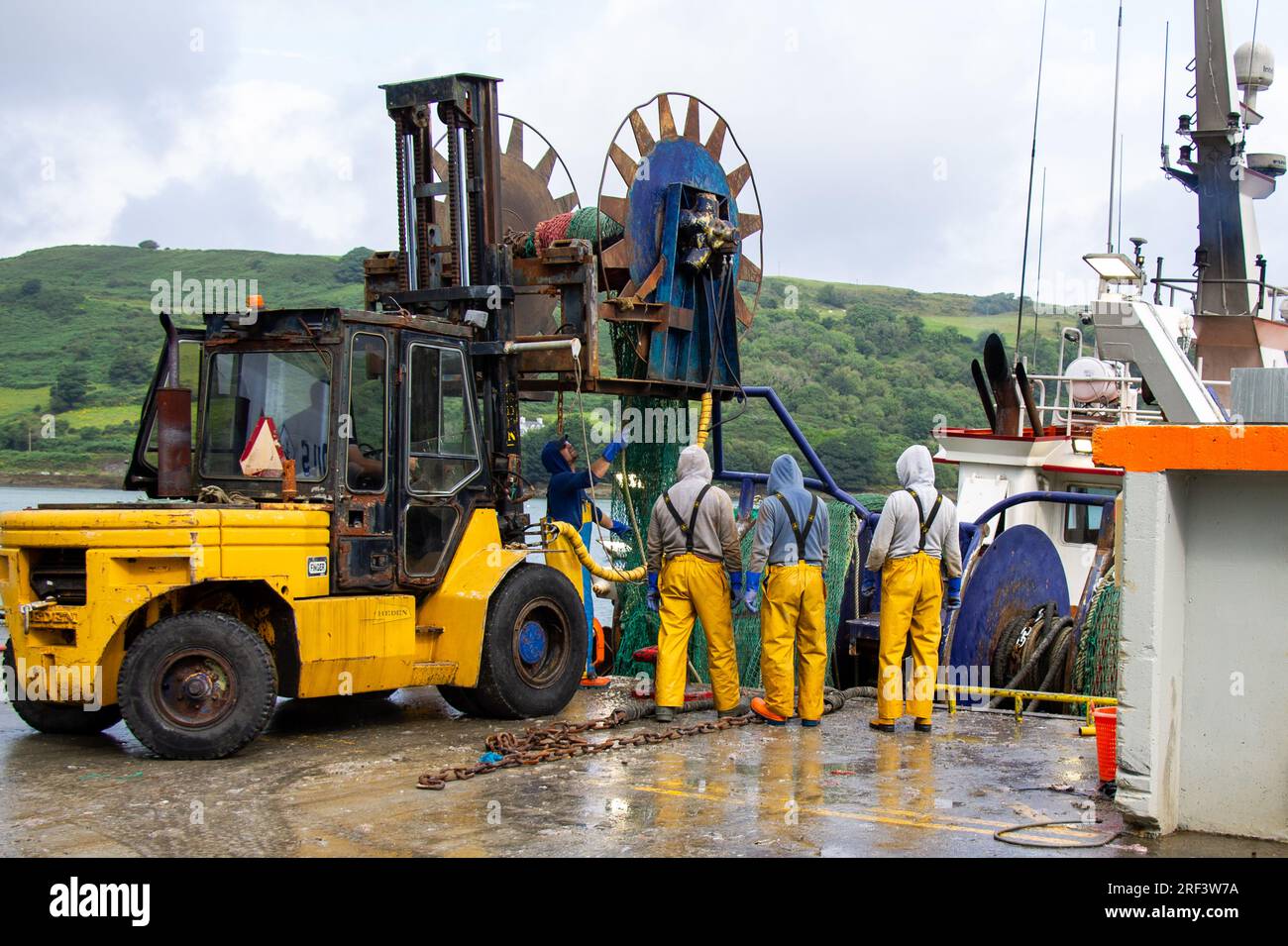 Fischer, die Netze mit Gabelstaplern und hydraulischen Rollen auf einen Trawler laden. Stockfoto