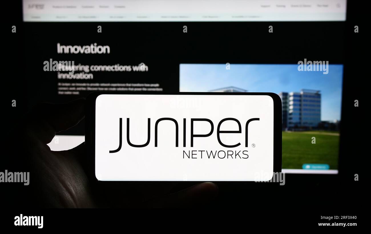 Person, die ein Mobiltelefon mit dem Logo des amerikanischen Hardwareunternehmens Juniper Networks Inc. Auf dem Bildschirm vor der Webseite hält. Konzentrieren Sie sich auf das Display des Telefons. Stockfoto