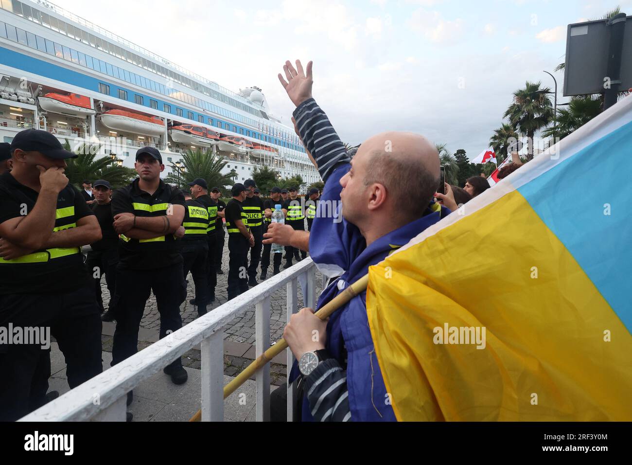 BATUMI, GEORGIEN - 31. JULI 2023 - Ein Mann mit ukrainischer Flagge steht vor Polizeilinien, während Demonstranten gegen die Ankunft der Astoria Grande cr protestieren Stockfoto