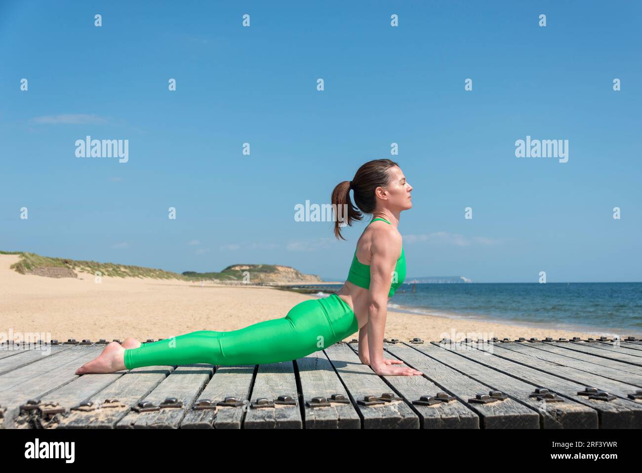 Eine weiße Frau, die am Meer mit dem Kopf nach oben schauende Hundehaltung vorführt. Stockfoto